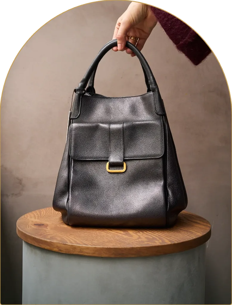 A black Delvaux leather bag, held above a wooden pedestal
